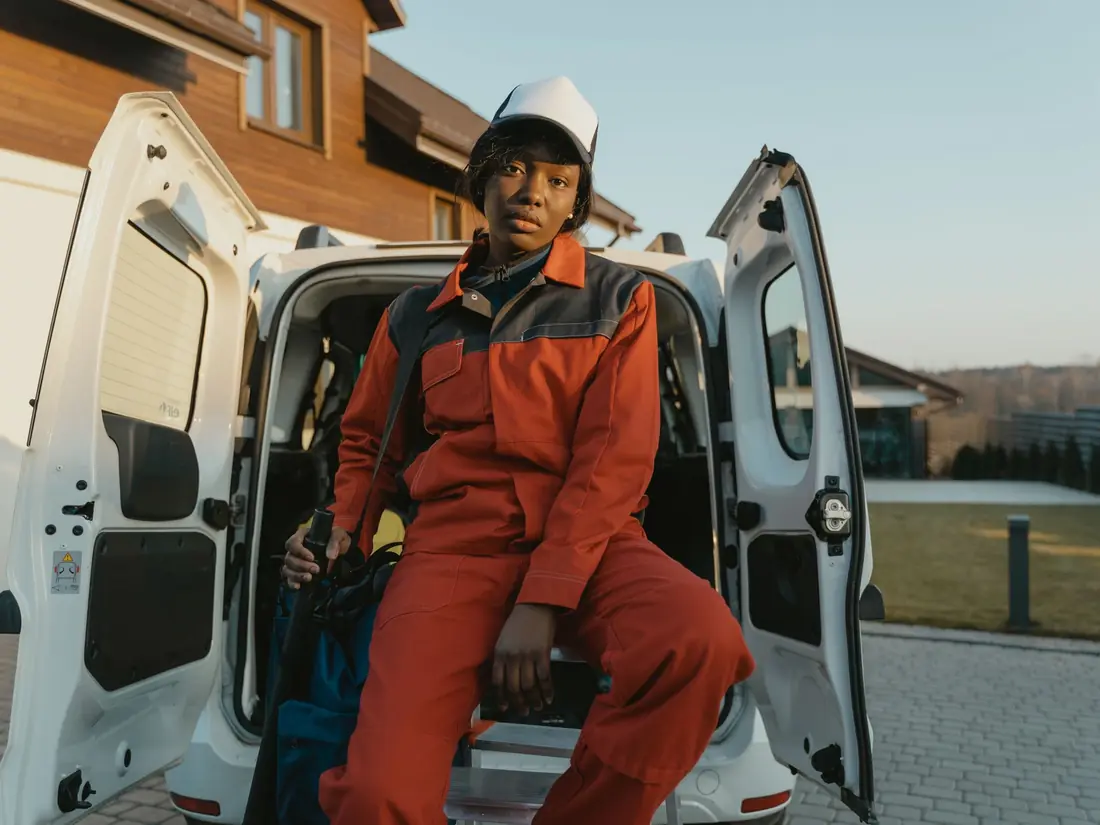A tradeswoman in orange workwear sitting in the back of her van at the end of the day
