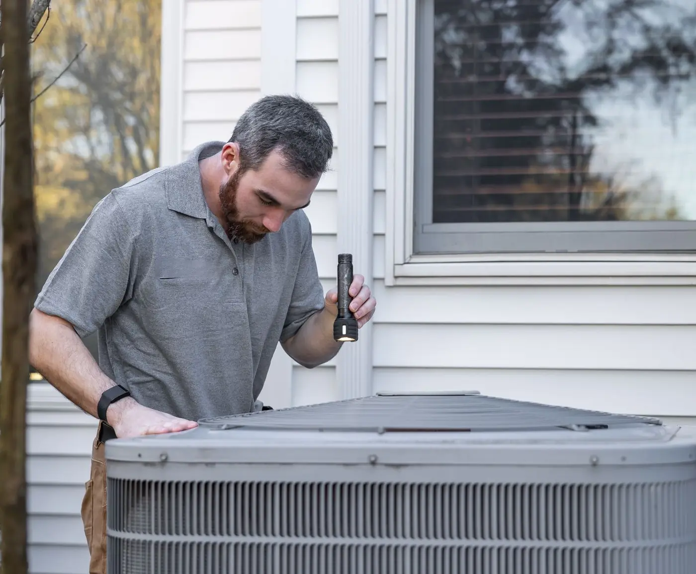 An HVAC technician checking an outdoor air-conditioning unit beside a customer's house