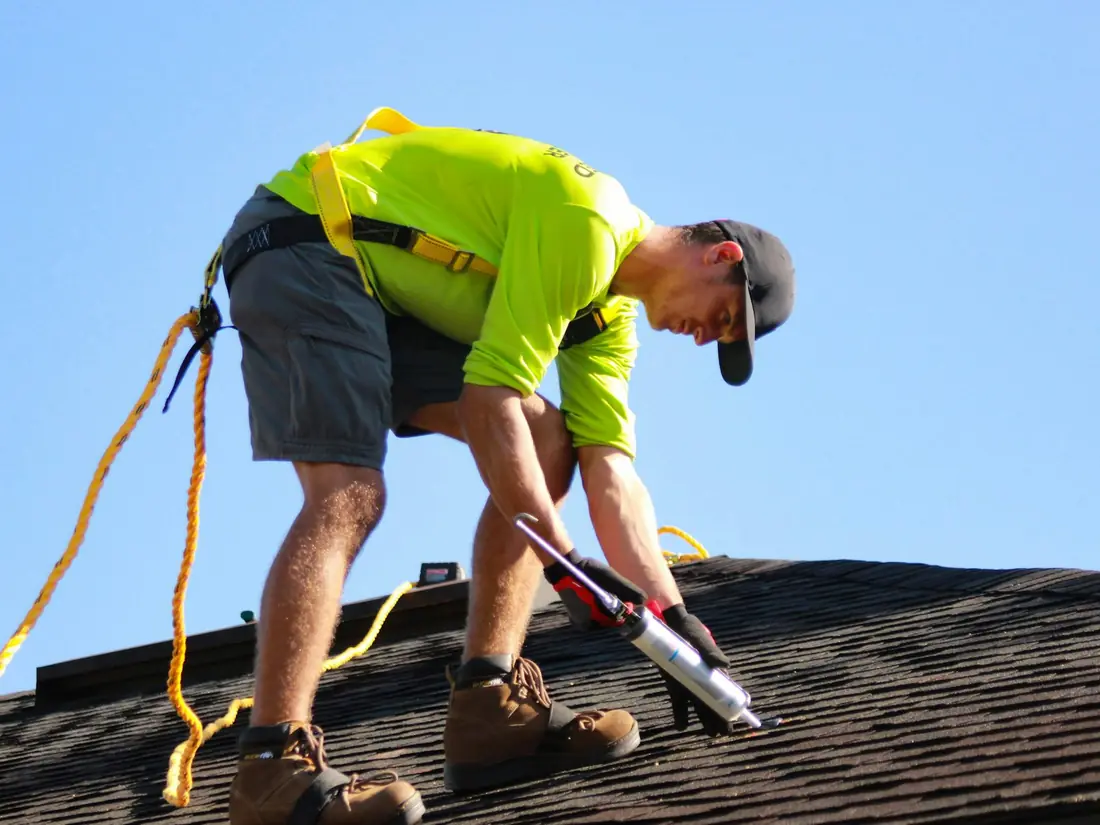 A roofer in a safety harness sealing shingles on a roof