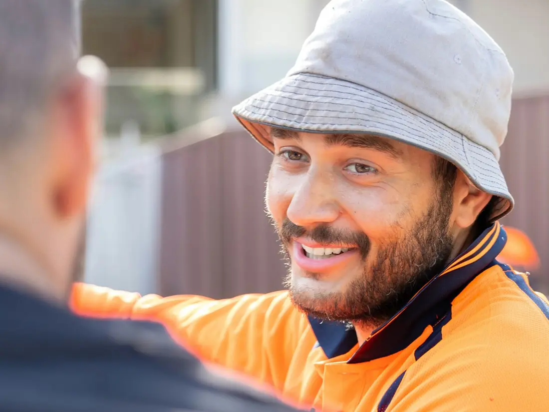 A tradesman in a hi-vis shirt smiling as he talks with a customer outside their house